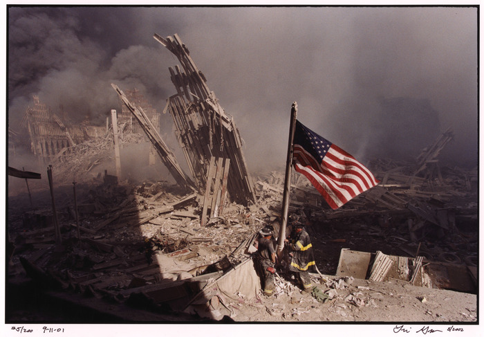 The Firemen and the Flag
On the morning of September 11, 2001, Lori Grinker, a professional photographer with the internationally renown agency, Contact Press Images, left her apartment in Williamsburg, Brooklyn. On her way to the subway, she glimpsed the Trade Centers on fire rising over the Brooklyn Queens Expressway. She began photographing. She quickly found her way to the Williamsburg Bridge, and walked all the way to the site of the attack at the World Trade Center where she spent several hours photographing the devastation. At approximately 3:30 pm she was standing in front of the bombed out windows on the second floor of Two World Financial Center when the three firefighters walked into her view and proceeded to raise the American flag over the smoldering ruins.

Copyright
copyright, Lori Grinker, 2001